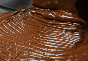 Image of freshly made melted chocolate in liquid form, pouring into a pan in a ribbon-like pattern